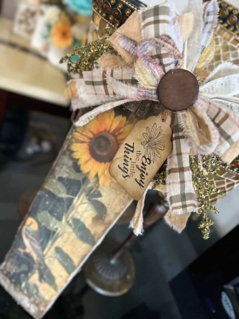 DIY Scrap wood sunflower decor with a free sunflower printable on rice paper, decoupaged onto a piece of scrap wood and a big messy fabric bow with a hangtag that says "enjoy the little things".