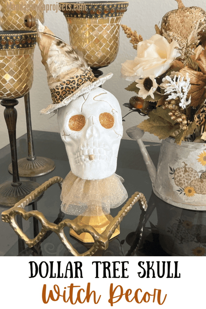 Dollar Tree plastic skull for Halloween, painted white with gold glitter eyes on top of a gold candlestick with a gold tulle neck collar and a witches that was redone with neutral and leopard print fabric and a feather in it's hat.