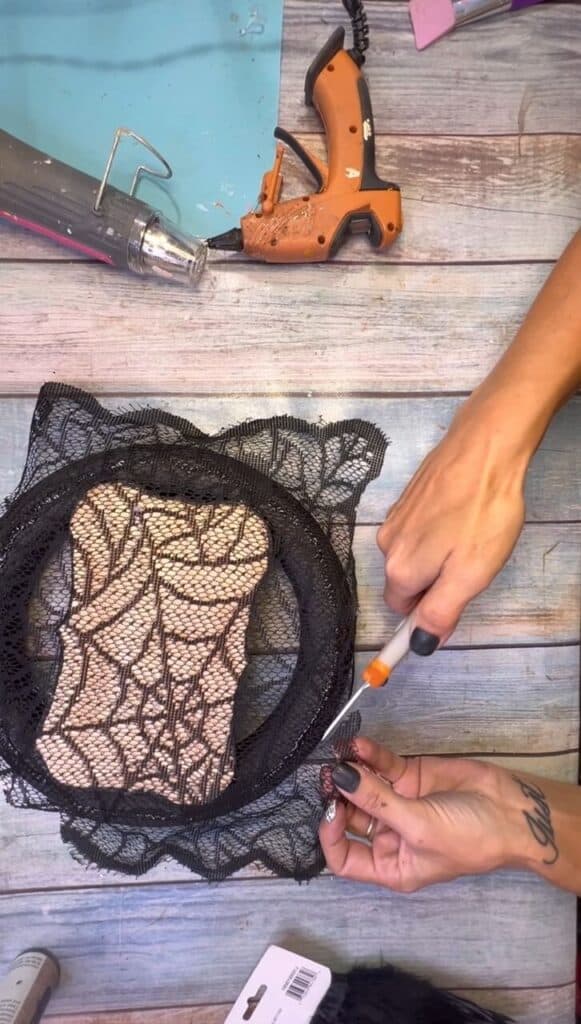 Cutting the excess black lace that hangs over the edge of the wreath form.