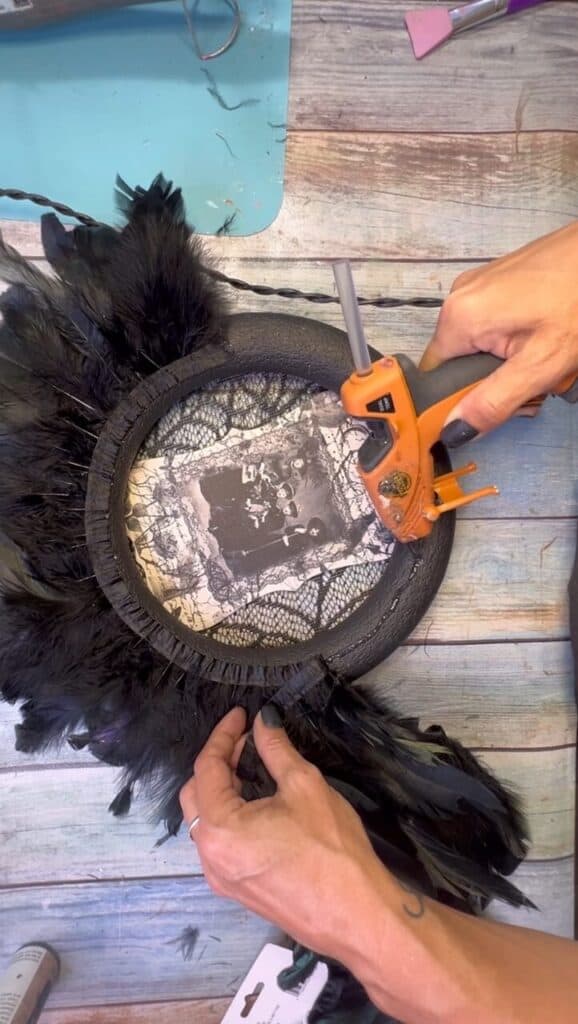 Gluing the black feather trim to the outside of the wreath form.