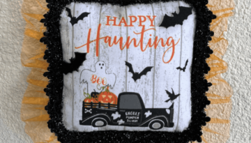 Dollar Tree Halloween Pot Holder with a Ghost, bats, and an old truck that says "Happy Haunting with orange tulle trim around the edge and a black and white buffalo check wood bead hanger, DIY doorknob hanger.