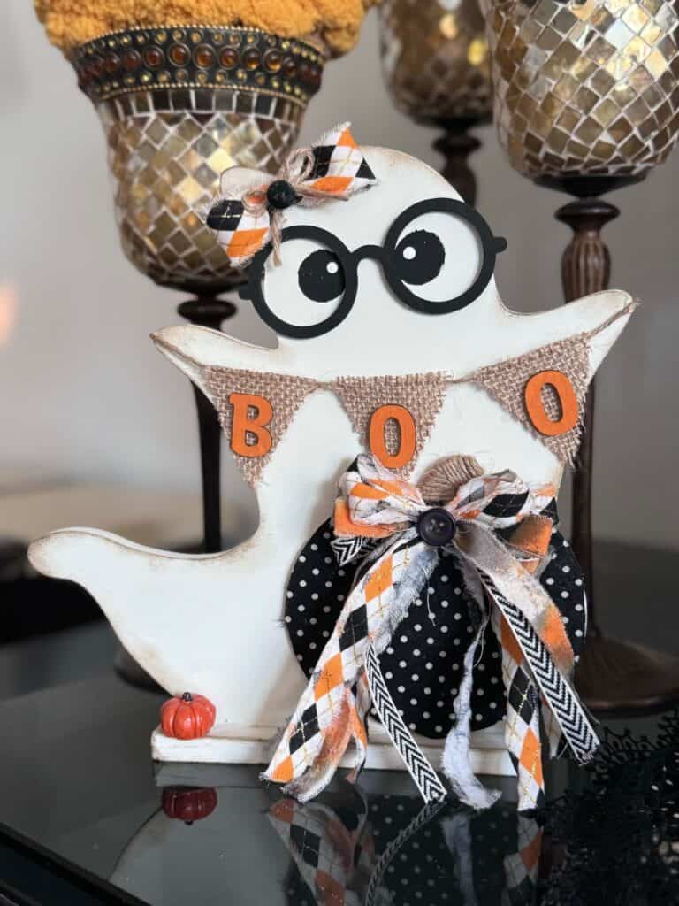 Cute thrifted wood standing ghost makeover with a black and white polka dot pumpkin, a burlap banner that says "BOO", black eyeglasses, and an orange and black fabric bow.