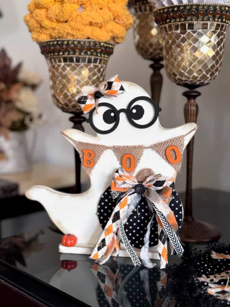 Cute thrifted wood standing ghost makeover with a black and white polka dot pumpkin, a burlap banner that says "BOO", black eyeglasses, and an orange and black fabric bow.