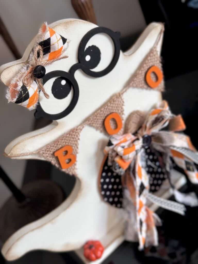 Cute thrifted wood standing ghost makeover with a black and white polka dot pumpkin, a burlap banner that says "BOO", black eyeglasses, and an orange and black fabric bow.