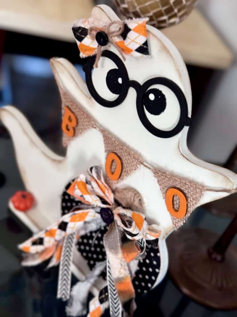 Cute thrifted wood standing ghost makeover with a black and white polka dot pumpkin, a burlap banner that says "BOO", black eyeglasses, and an orange and black fabric bow.