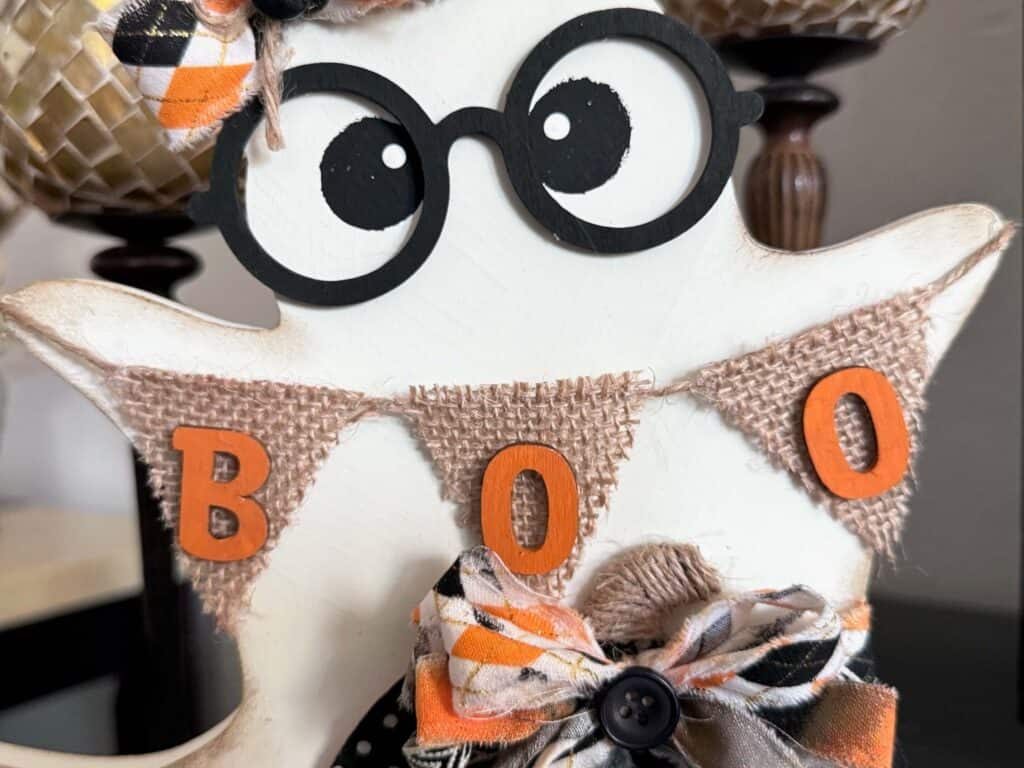 The ghost holding a burlap banner that says "BOO" in orange letters.