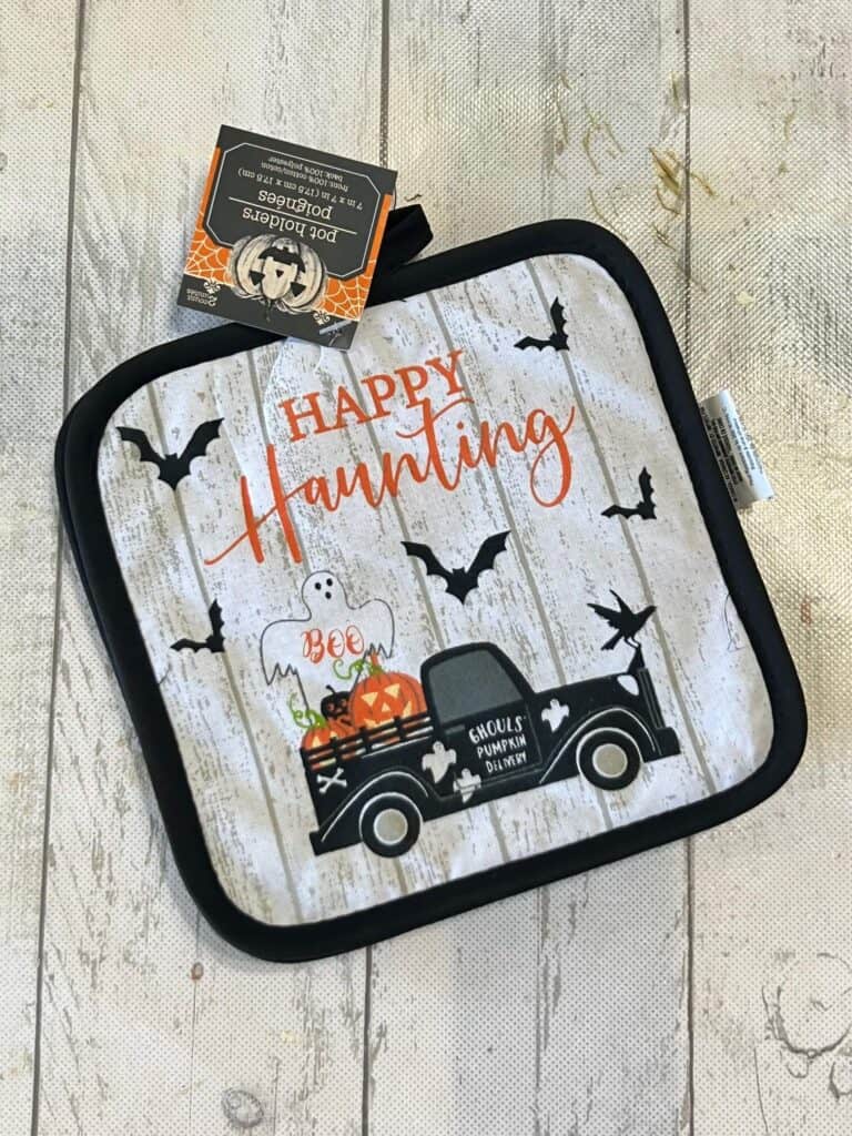 Dollar Tree Halloween Pot Holder with a Ghost, bats, and an old truck  with pumpkins in the back that says "Happy Haunting.