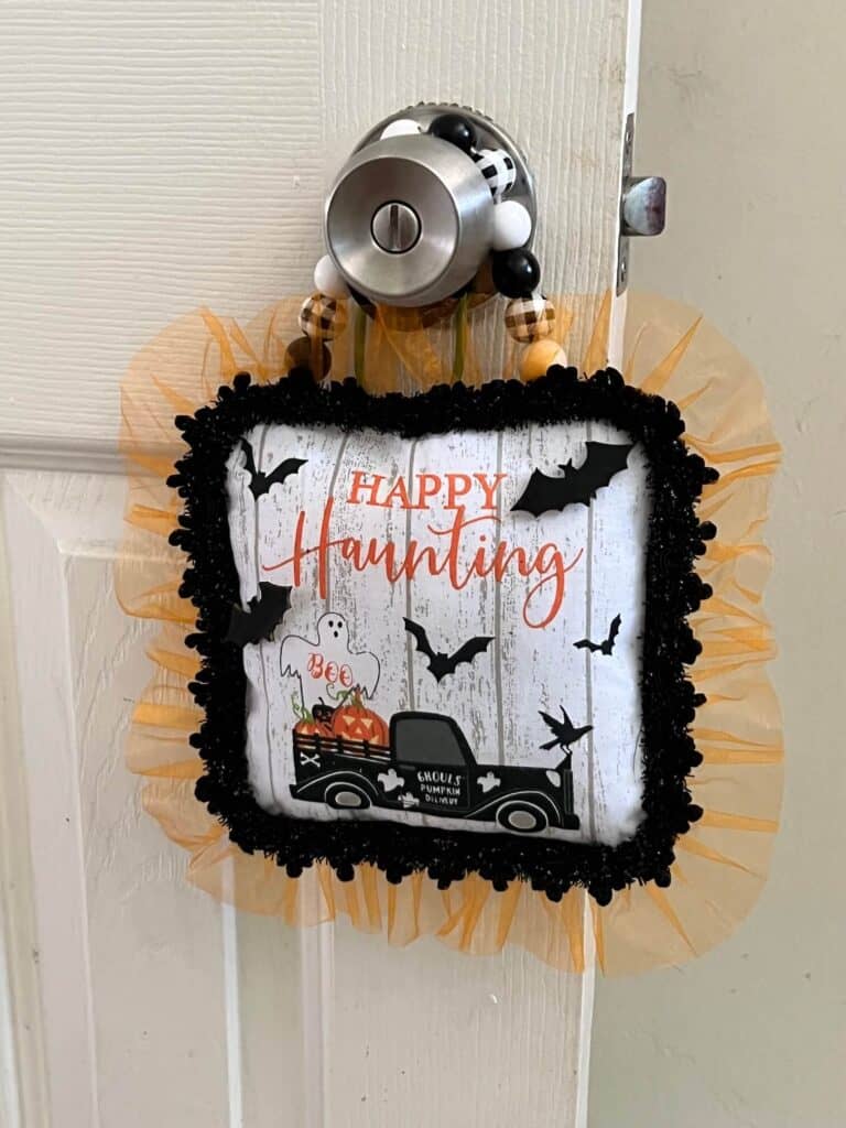 Dollar Tree Halloween Pot Holder with a Ghost, bats, and an old truck that says "Happy Haunting with orange tulle trim around the edge and a black and white buffalo check wood bead hanger, DIY doorknob hanger.