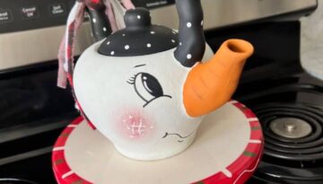 Thrifted Hand painted snowman teapot with the "spout" painted orange as the "carrot" nose, big black eyed, rosy pink cheeks, black and white polka dot handle, and a black, red, and white scrappy fabric bow on the handle.