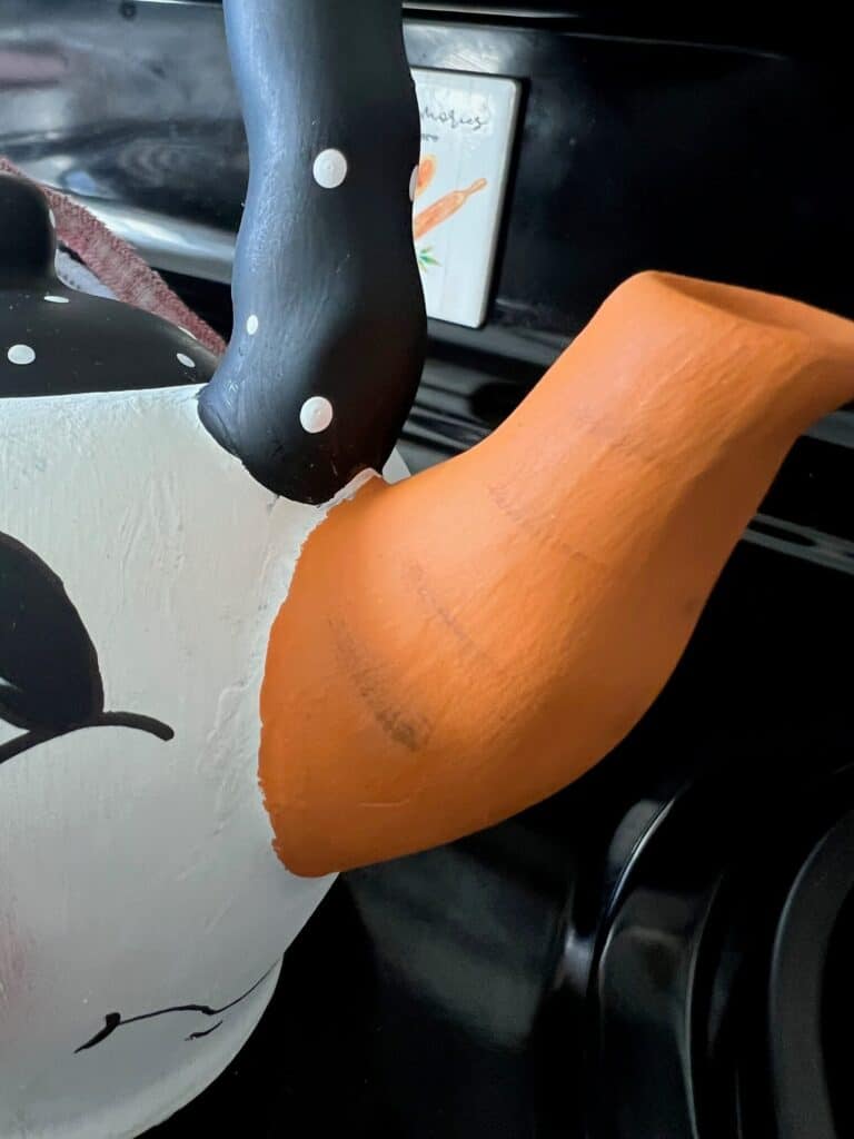 The spout of the teapot painted orange with brown lines to look like a carrot.