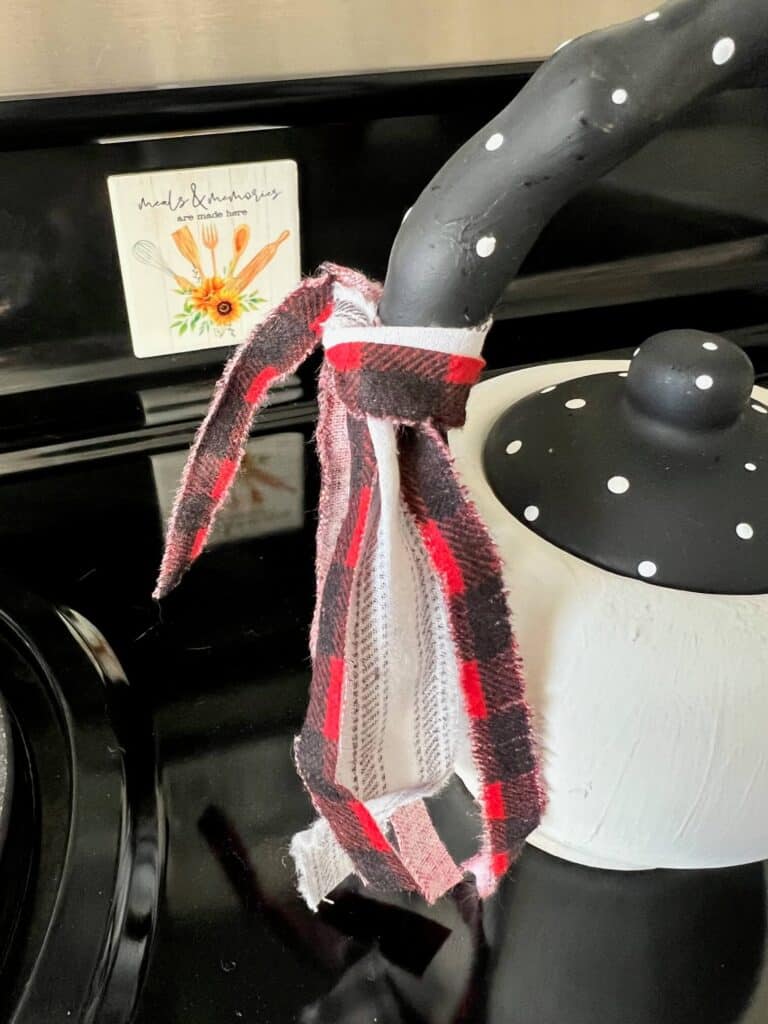 Scrappy red white and black fabric bow tied to the handle of the teapot.