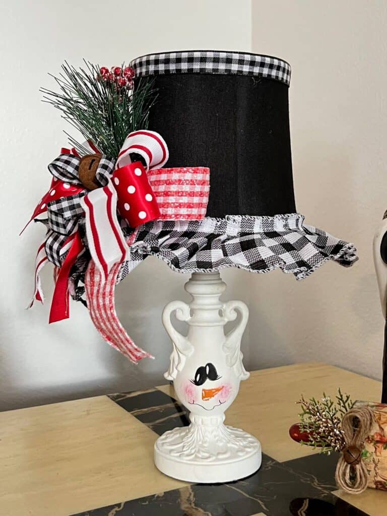 Turn and ordinary thrift store small lamp into adorable and budget friendly Christmas and Winter decor by painting it to look like a snowman. With the lampshade being the "top hat" with a cute red, black, and white bow and a jingle bell, and the lamp body painted like a snowman face. 