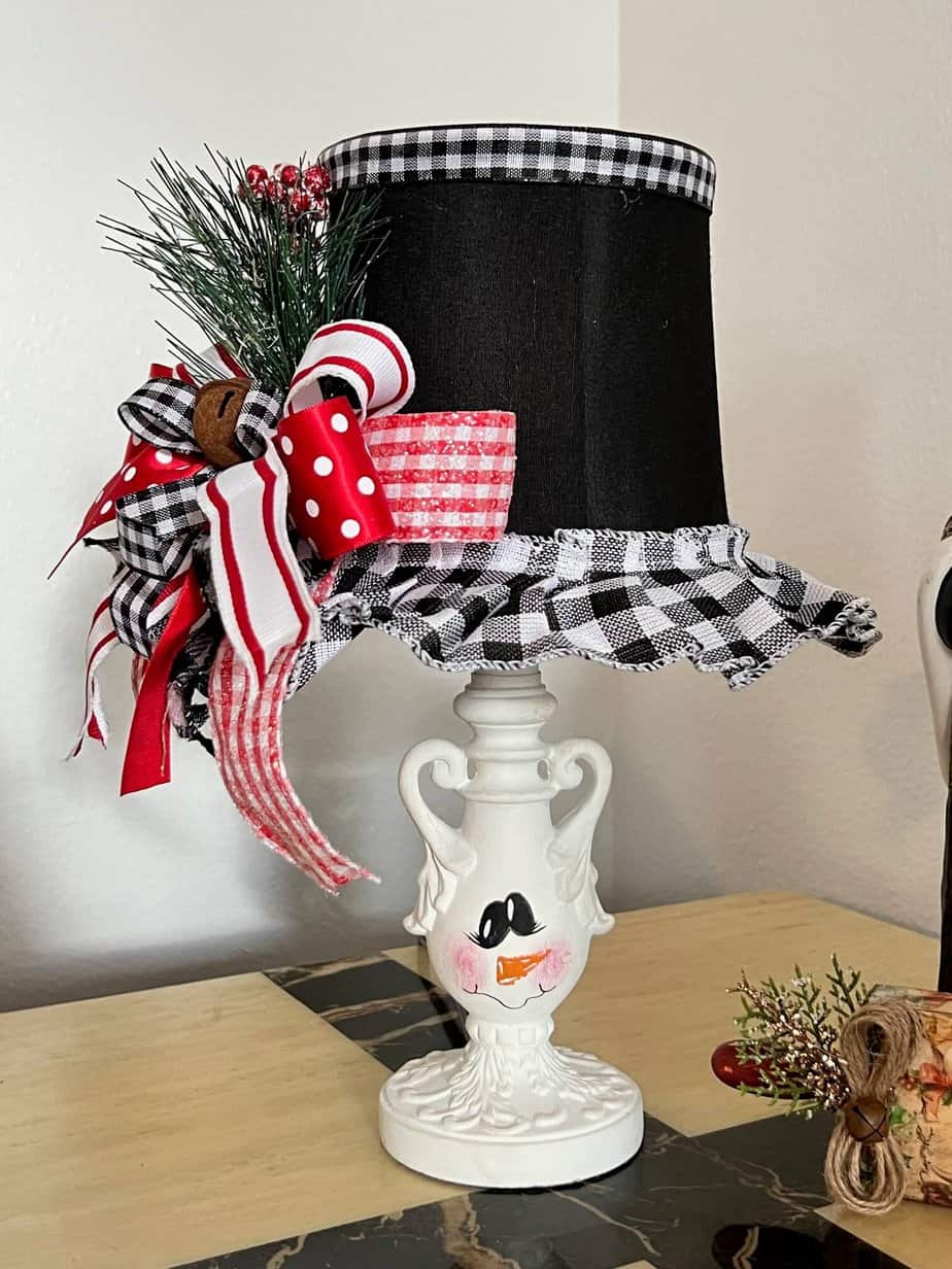 Turn and ordinary thrift store small lamp into adorable and budget friendly Christmas and Winter decor by painting it to look like a snowman. With the lampshade being the "top hat" with a cute red, black, and white bow and a jingle bell, and the lamp body painted like a snowman face.