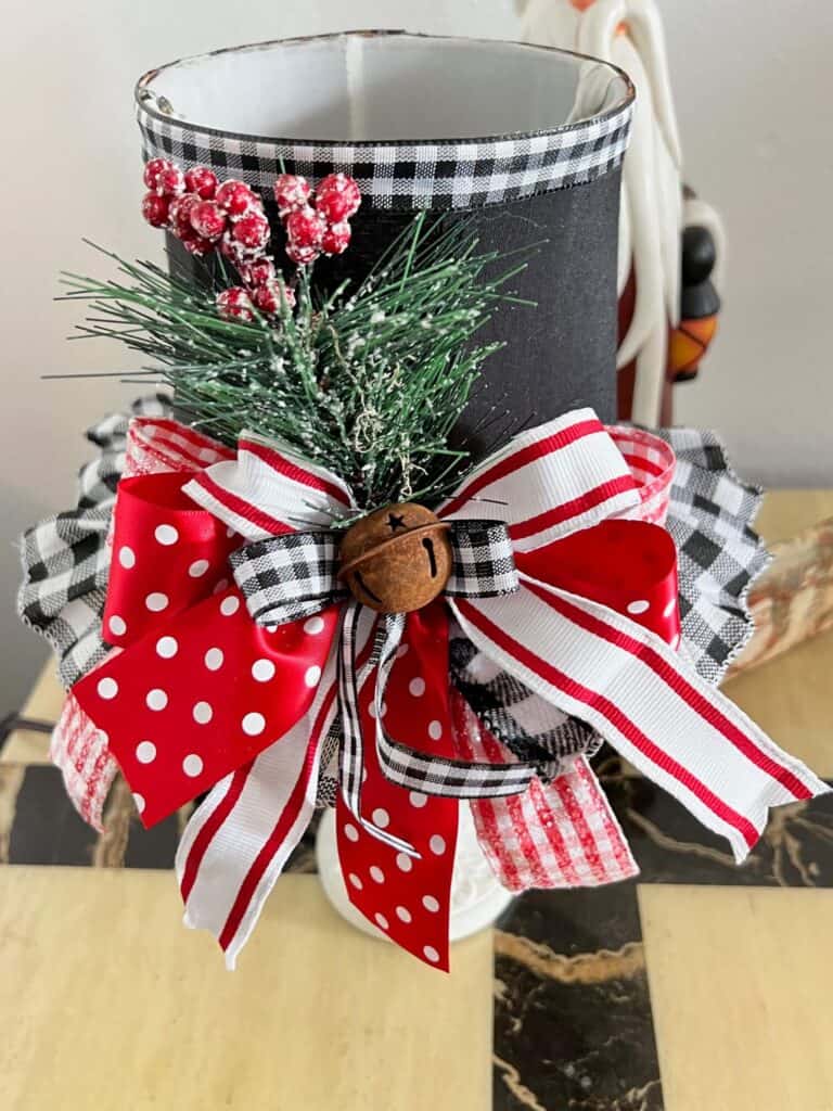 A huge black red and white bow with a rusty bell and greenery and red berries.