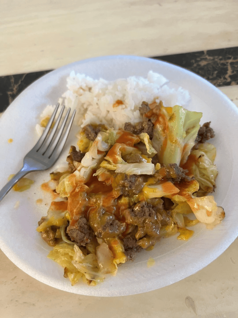 Cabbage casserole on a plate with white rice and franks red hot sauce on top.