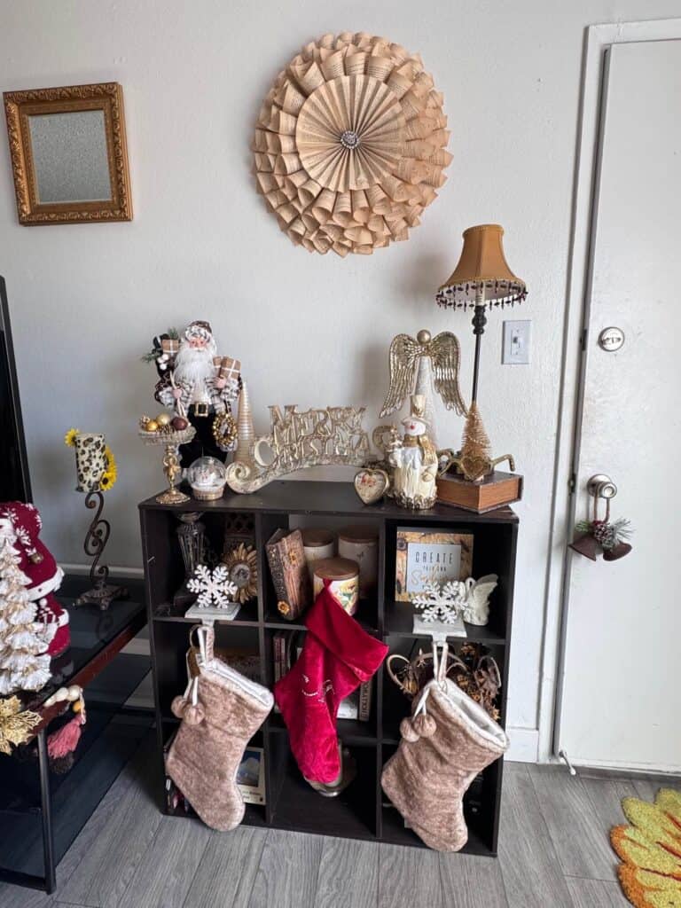 Bookcase decorated with all gold and white christmas decor and 3 stockings hung below.