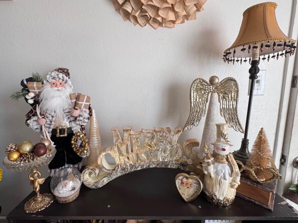 The top of a bookcase decorated with gold and white Christmas decor with a leopard print santa, snowman, Angel, and Merry Christmas Sign.