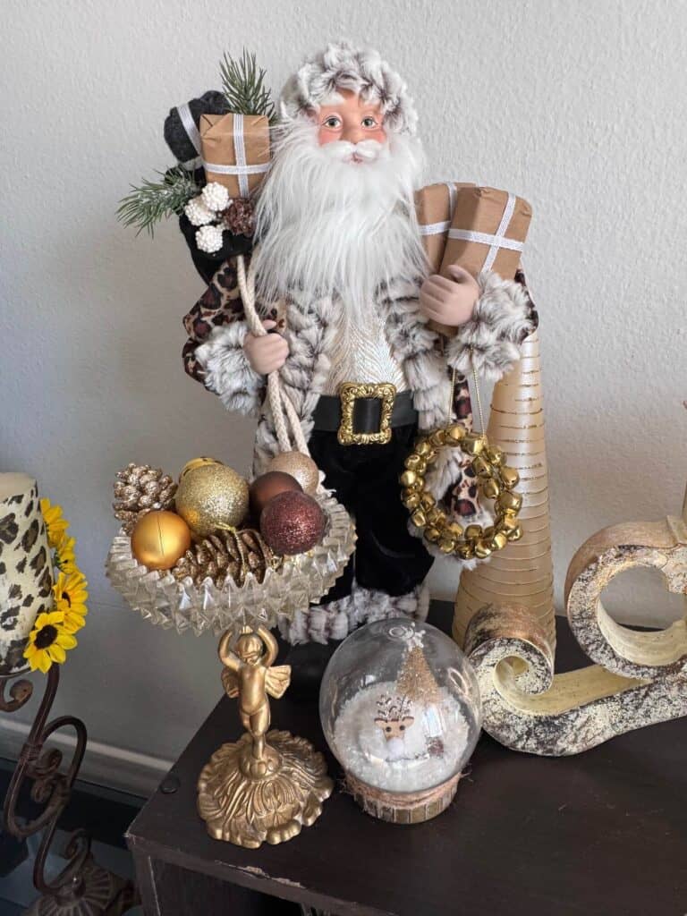 Leopard print Santa and a thrifted candy dish with gold ornaments and pine cones, and a reindeer snow globe.