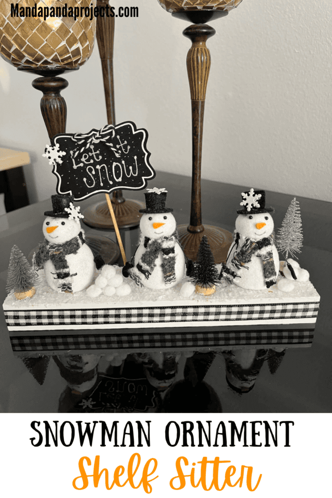 Snowmen Ornament Shelf sitter made with 3 mini felt white snowmen from walmart, on a wood base with a chalkboard sign that says "let it snow", snowballs made with white pom poms, and black and silver bottle brush christmas trees.