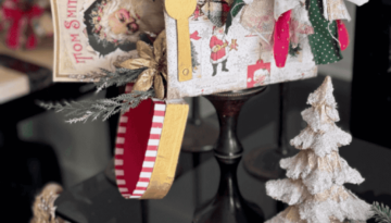 A dollar tree penguin cardboard mailbox that was made over for Christmas with a vintage santa napkin, some gold poinsettias, christmas greenery, and a messy fabric bow on a wood candlestick base for DIY decor.