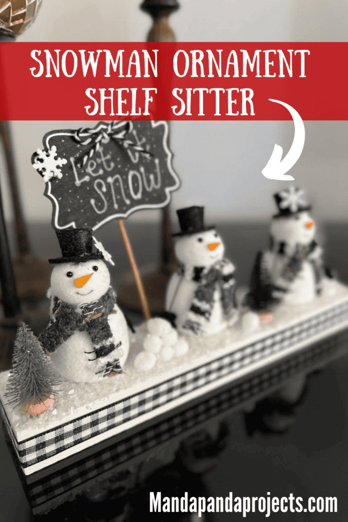 Snowmen Ornament Shelf sitter made with 3 mini felt white snowmen from walmart, on a wood base with a chalkboard sign that says "let it snow", snowballs made with white pom poms, and black and silver bottle brush christmas trees.