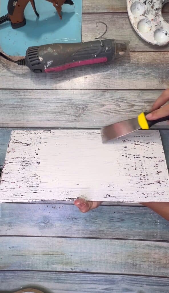 Using a paint scraper to scrape of the white paint and make it look chippy.