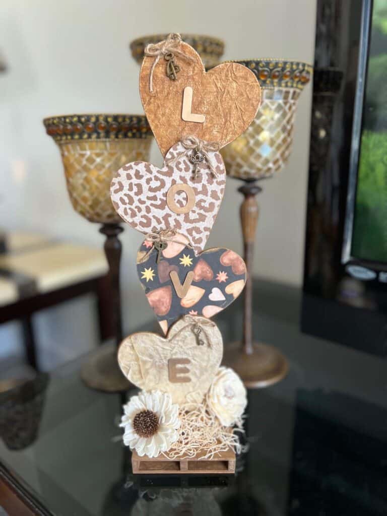 Neutral Stacked Hearts with the word LOVE in gold with leopard print, brown, and creme colors and sola wood flowers at the bottom. The hearts have a twine bow with skeleton key on each of them, perfect for Decor for Valentines Day.