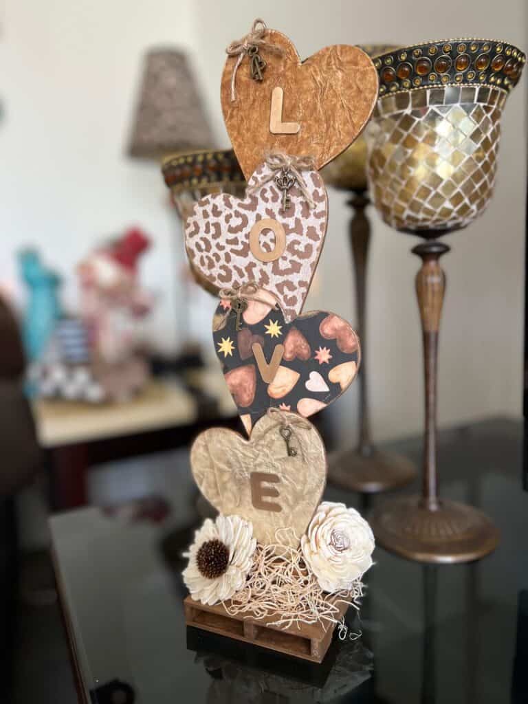 Neutral Stacked Hearts with the word LOVE in gold with leopard print, brown, and creme colors and sola wood flowers at the bottom. The hearts have a twine bow with skeleton key on each of them, perfect for Decor for Valentines Day.