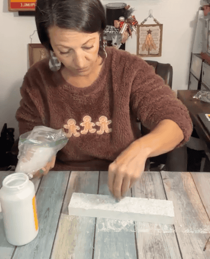 Sprinkling faux snow on the painted white wood base of the shelf sitter.