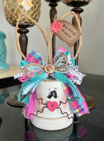 White Terra Cotta Pot Bunny with wired jute ears, a pink, purple, and teal messy fabric bow and a cute tag on her ear that says "bunny love" for spring and easter crafts and decor.