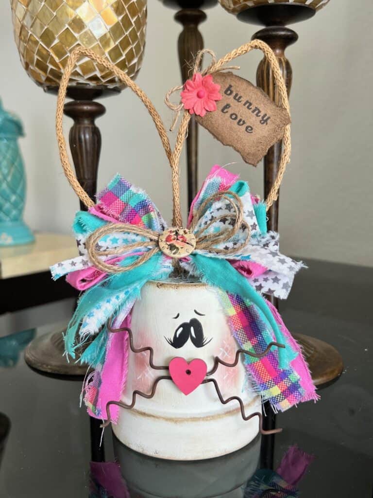 White Terra Cotta Pot Bunny with wired jute ears, a pink, purple, and teal messy fabric bow and a cute tag on her ear that says "bunny love" for spring and easter crafts and decor. 