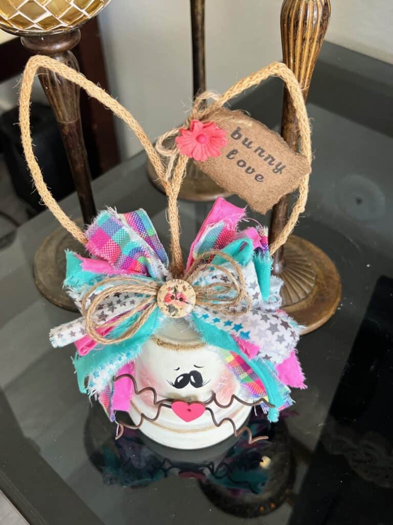 White Terra Cotta Pot Bunny with wired jute ears, a pink, purple, and teal messy fabric bow and a cute tag on her ear that says "bunny love" for spring and easter crafts and decor. 