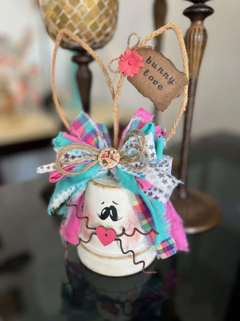 White Terra Cotta Pot Bunny with wired jute ears, a pink, purple, and teal messy fabric bow and a cute tag on her ear that says "bunny love" for spring and easter crafts and decor. 