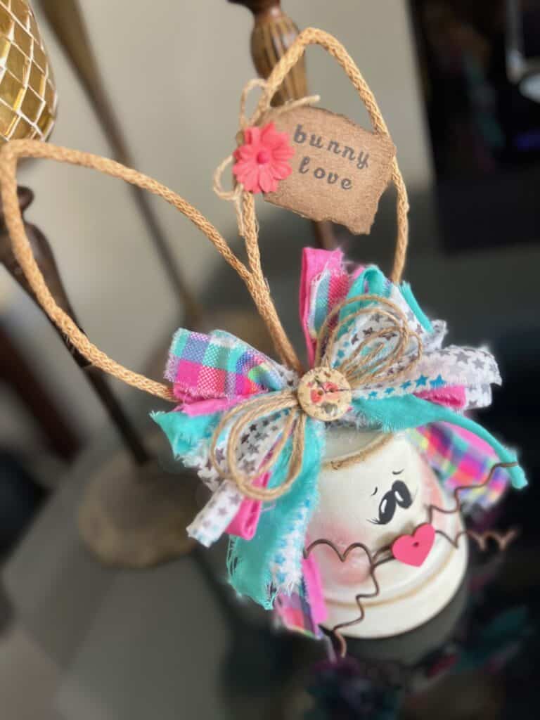 White Terra Cotta Pot Bunny with wired jute ears, a pink, purple, and teal messy fabric bow and a cute tag on her ear that says "bunny love" for spring and easter crafts and decor. 