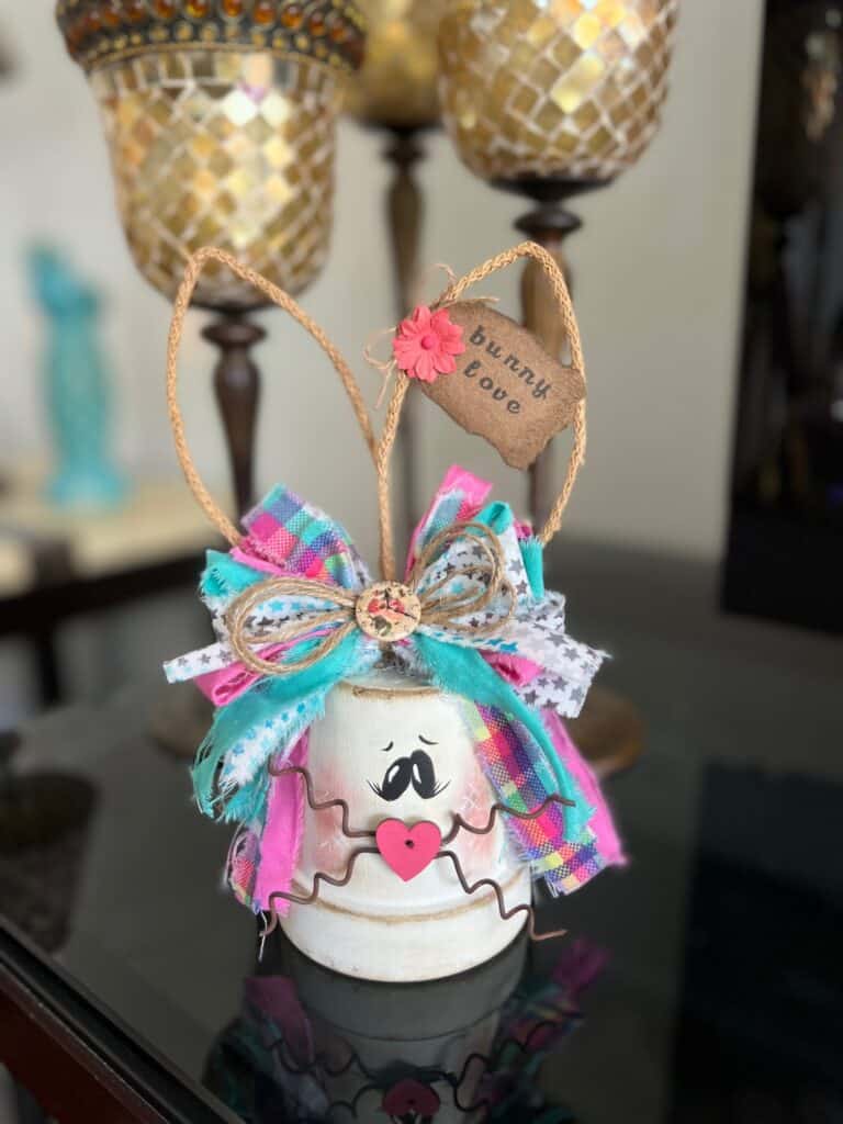 White Terra Cotta Pot Bunny with wired jute ears, a pink, purple, and teal messy fabric bow and a cute tag on her ear that says "bunny love" for spring and easter crafts and decor. 