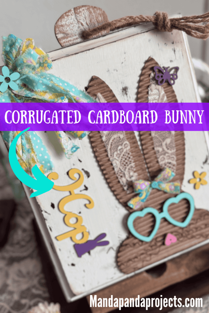 Corrugated cardboard bunny with messy fabric bow with purple, teal and yellow, with teal heart shaped glasses, a heart nose, butterflies, flowers, and a Dollar Tree bunny Hop sign, on a chippy white background.