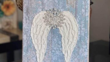 A Dollar Tree stretch canvas with pretty distressed blue scrapbook paper, a textured set of angel wings made with joint compound, sparkling with diamond dust and a totally dazzled bling in the center of the wings. A loving memory craft.