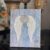 A Dollar Tree stretch canvas with pretty distressed blue scrapbook paper, a textured set of angel wings made with joint compound, sparkling with diamond dust and a totally dazzled bling in the center of the wings. A loving memory craft.