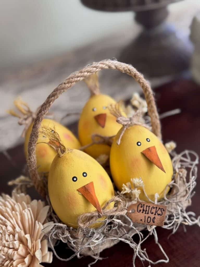 Wood easter eggs made into cute lil yellow peeps chicks in a recycled egg carton with spanish moss and a tag that says "Chicks .10 c" and a jute rope handle.