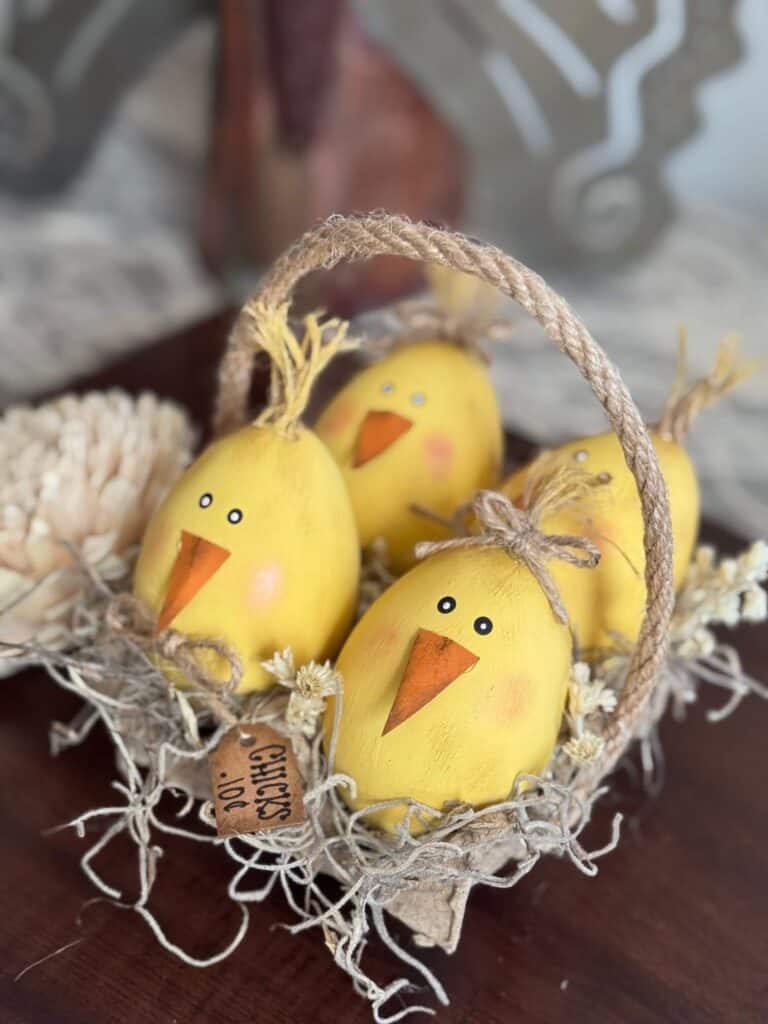 Wood easter eggs made into cute lil yellow peeps chicks in a recycled egg carton with spanish moss and a tag that says "Chicks .10 c" and a jute rope handle.