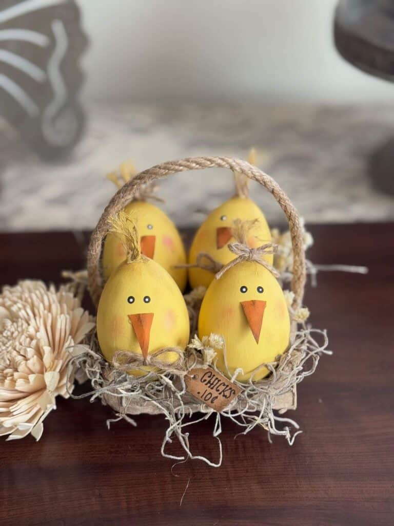 Wood easter eggs made into cute lil yellow peeps chicks in a recycled egg carton with spanish moss and a tag that says "Chicks .10 c" and a jute rope handle.