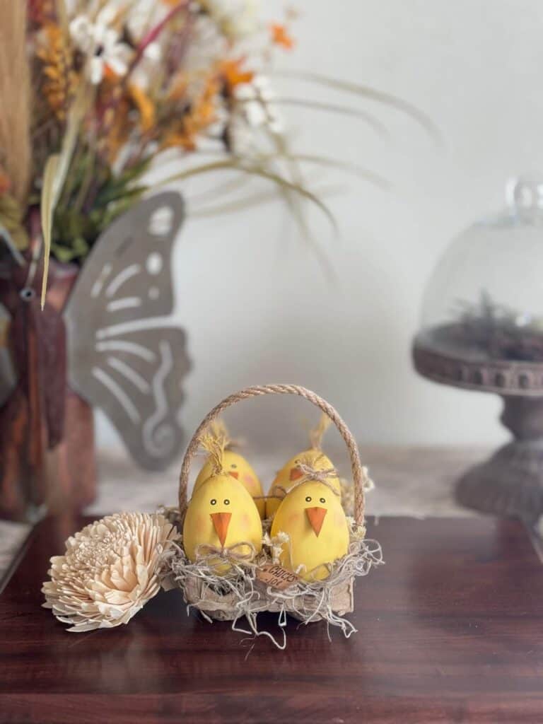 Wood easter eggs made into cute lil yellow peeps chicks in a recycled egg carton with spanish moss and a tag that says "Chicks .10 c" and a jute rope handle.