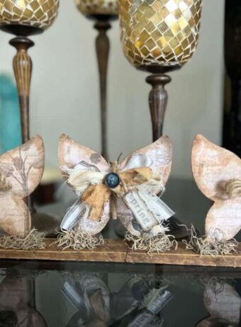 3 Wood Butterfly shelf sitter with a vintage vibe with a spring hangtag and twine and fabric bows, sitting on a base with spanish moss.