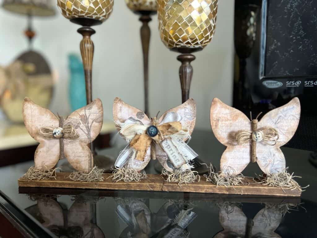 3 Wood Butterfly shelf sitter with a vintage vibe with a spring hangtag and twine and fabric bows, sitting on a base with spanish moss.