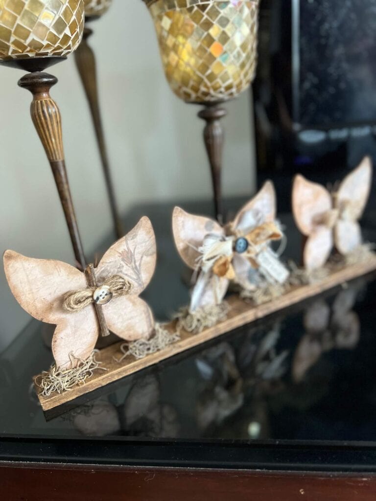 3 Wood Butterfly shelf sitter with a vintage vibe with a spring hangtag and twine and fabric bows, sitting on a base with spanish moss.