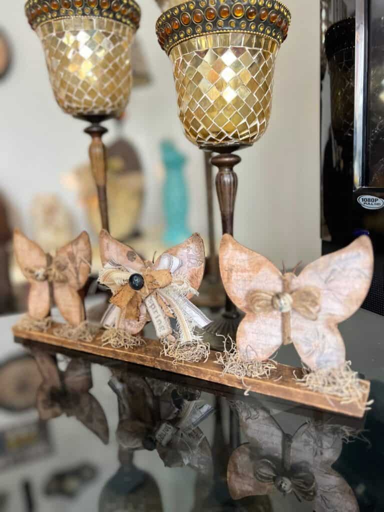 3 Wood Butterfly shelf sitter with a vintage vibe with a spring hangtag and twine and fabric bows, sitting on a base with spanish moss.