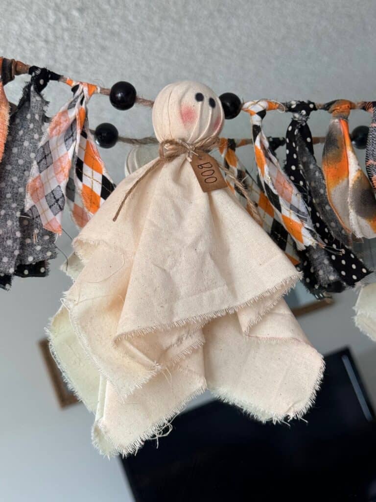 Muslin ghost with a hangtag around its neck that says "Boo" and orange and black fabric on each side.