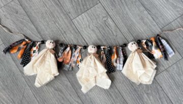 handmade Halloween Muslin Ghost Rag Garland features adorable fabric ghosts crafted from muslin cloth, accented with black wooden beads and festive rag ties in orange, black, and white patterns.