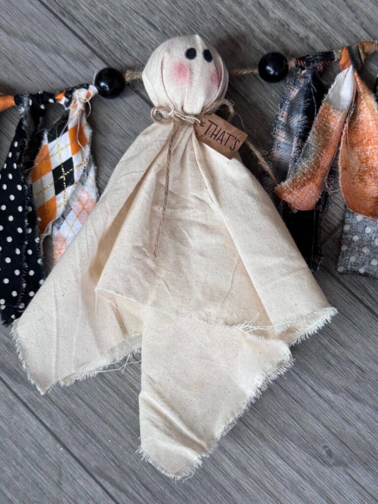 Muslin ghost with a hangtag around its neck that says "THATS" and orange and black fabric on each side.