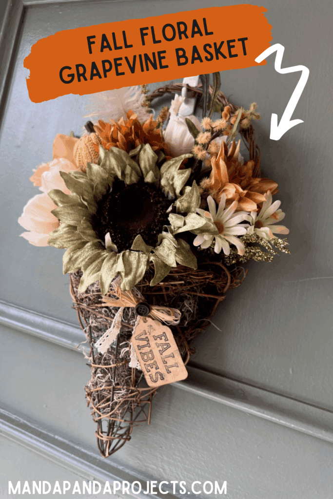 Fall floral grapevine wreath basket door decor hanging on a sage green front door with pretty fall flowers, a sweater pumpkin pick and a hangtag that says "Fall vibes".